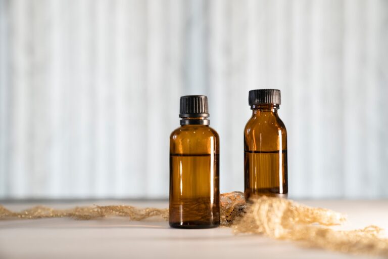 Person using a dropper to add essential oil to a small glass diffuser on a wooden table indoors.